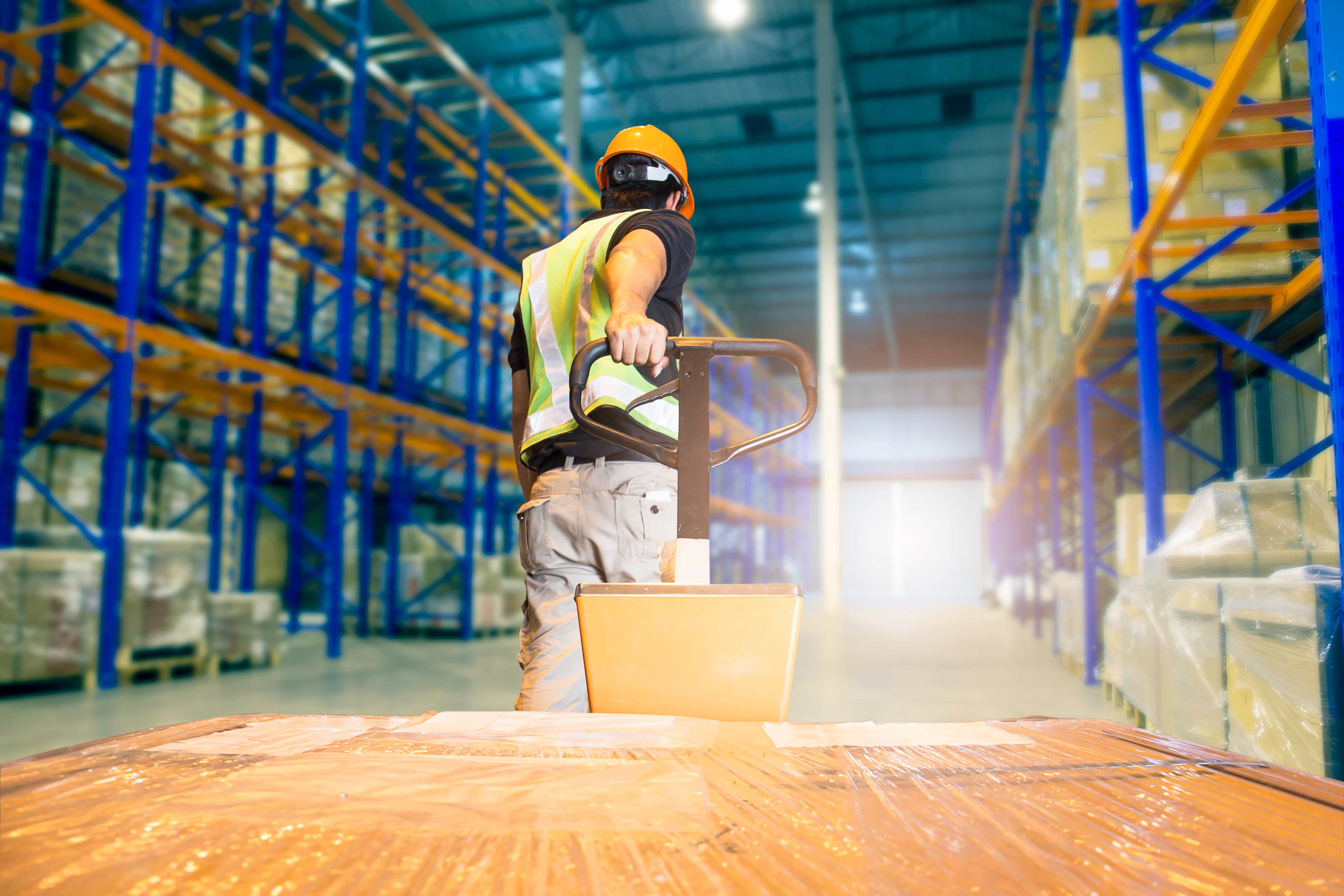 Worker pulling pallets of product in warehouse